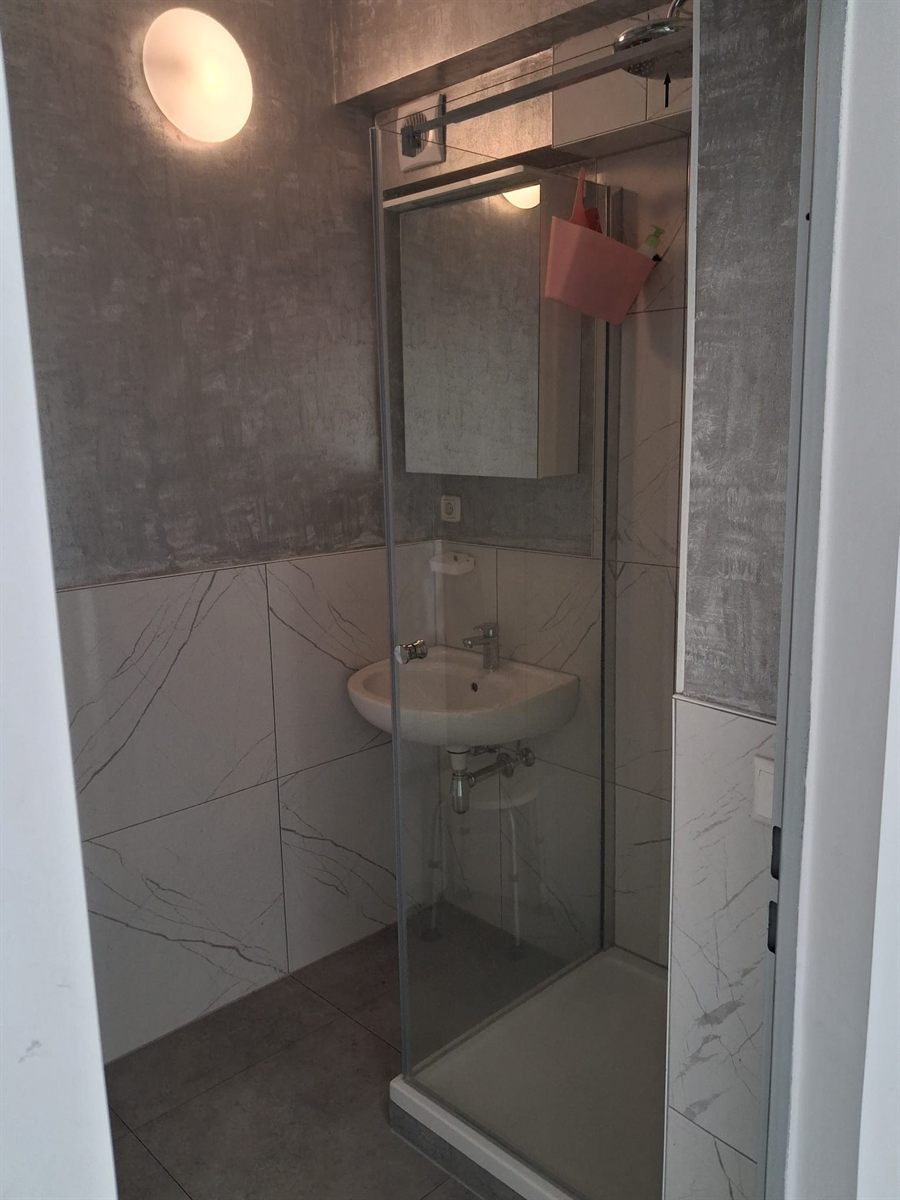 Gefliestes Gemeinschaftsbad mit Duschkabine, Waschbecken und Spiegelschrank