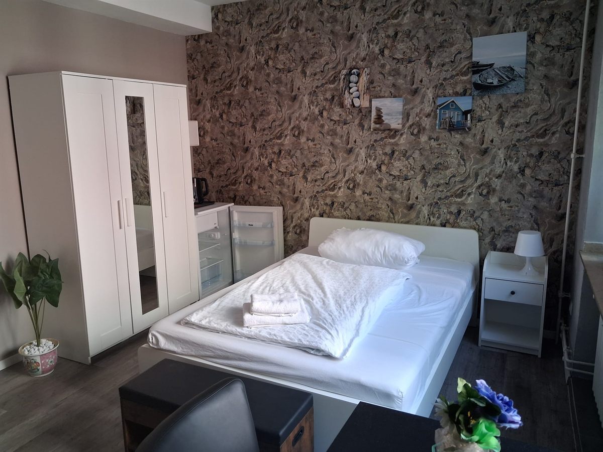 Einzelzimmer mit Bett, Kleiderschrank, Kühlschrank und Wasserkocher